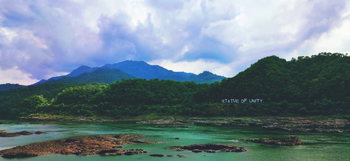 green mountain beside body of water under cloudy sky during daytime